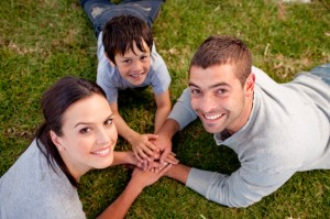 Parents and kid lying on garden with hands together