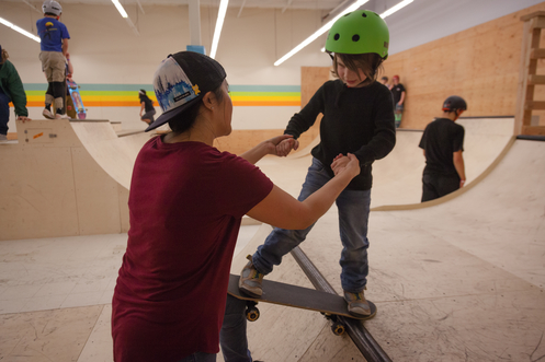 A coach helps a child learn to skateboard at Stronger Skatepark